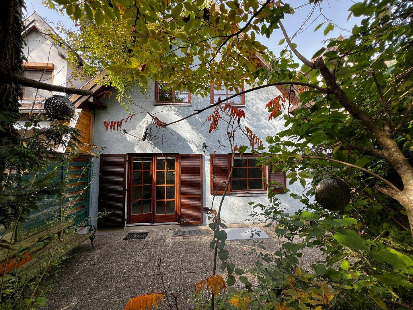 Rückansicht des Hauses mit Terrasse und üppiger Vegetation im Herbstlicht.