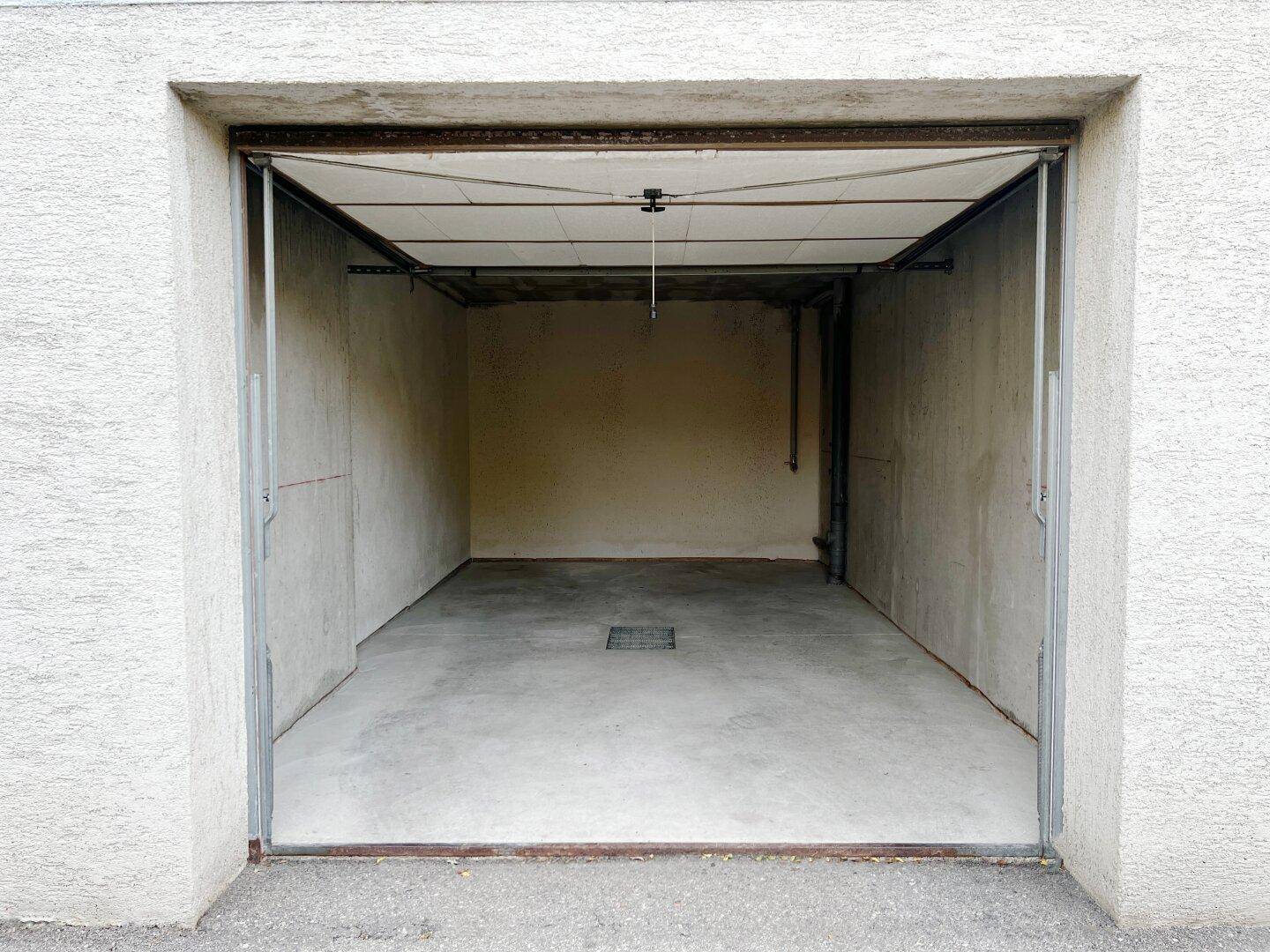 Leere Einzelgarage mit Betonboden und offenem Garagentor.
