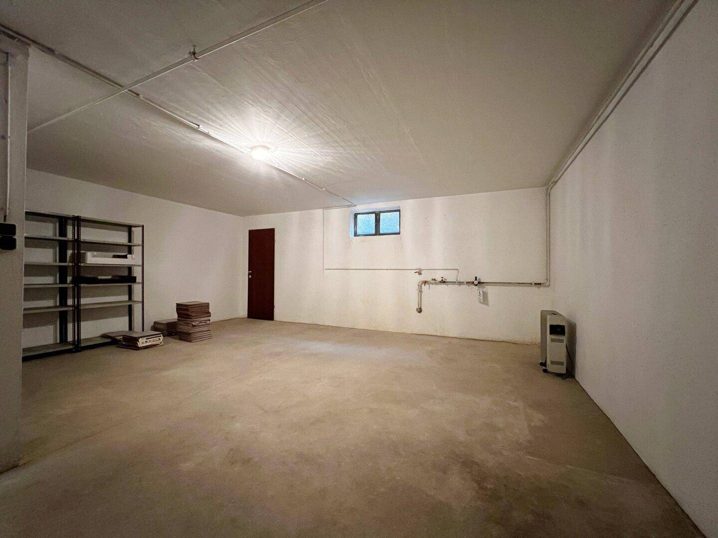 Geräumiger Kellerraum mit Betonboden, Regalen und kleinem Fenster, ideal als Abstellraum.