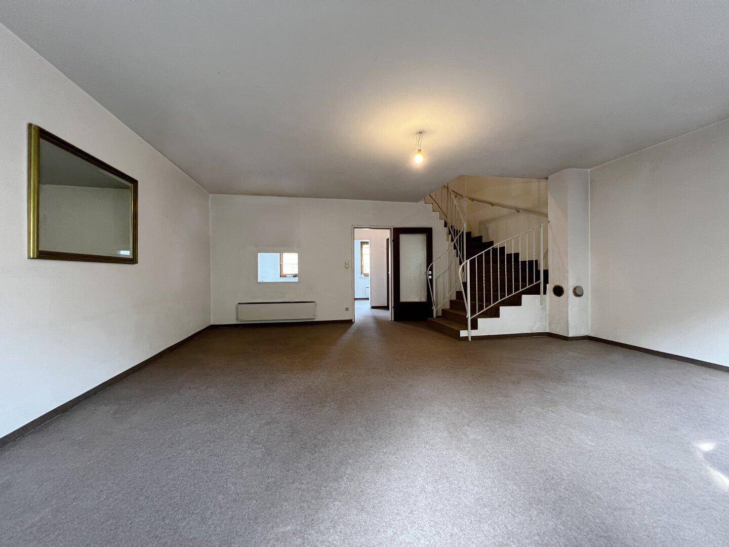 Wohnzimmer mit Teppichboden und einer Treppe, die in die oberen Stockwerke führt.