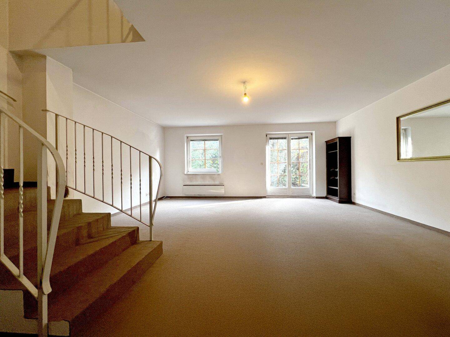 Helles Wohnzimmer mit Teppichboden, großen Fenstern und Zugang zur Terrasse.