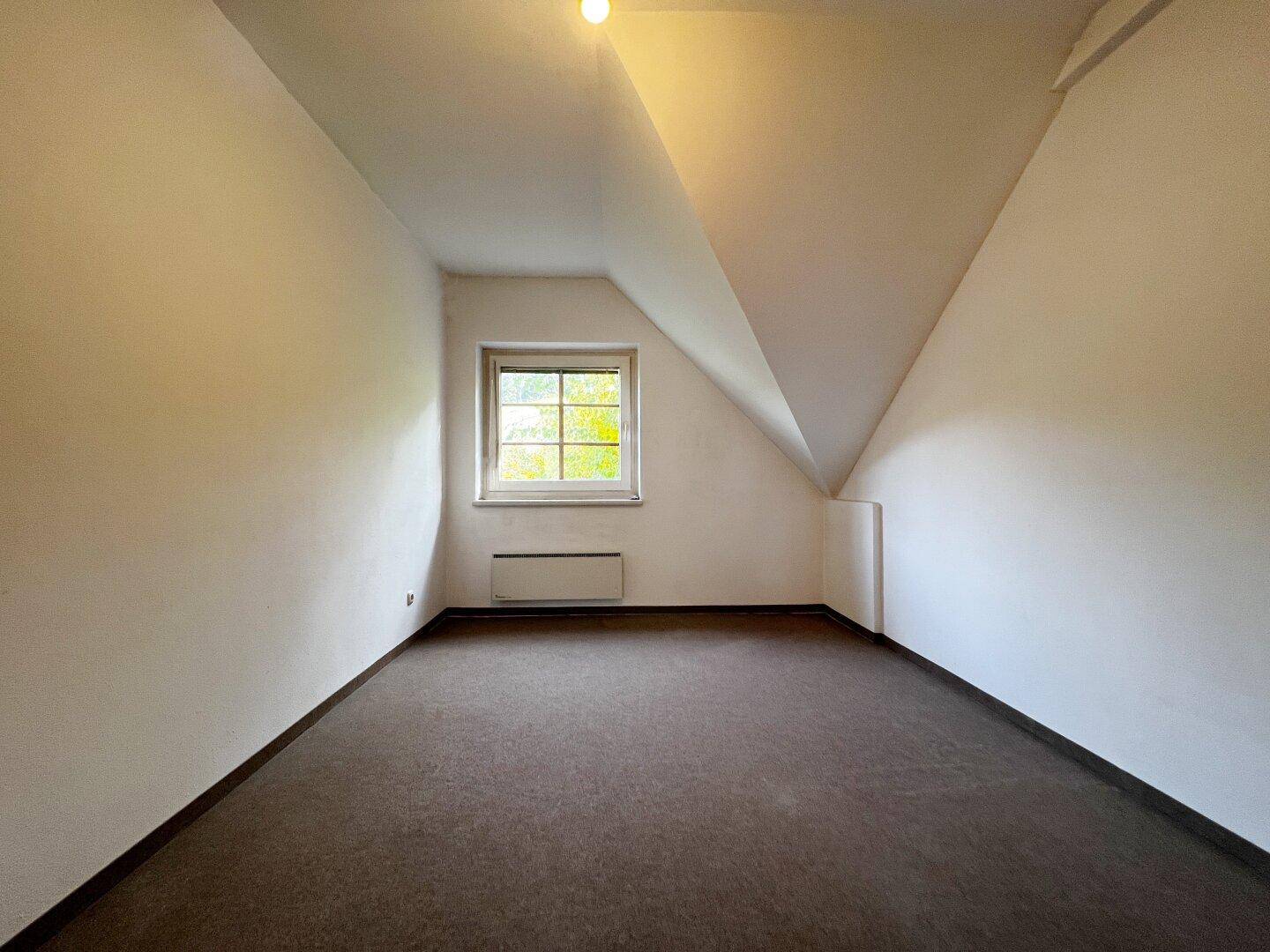 Helles Schlafzimmer im Dachgeschoss mit Teppichboden, schrägen Wänden und einem Fenster.