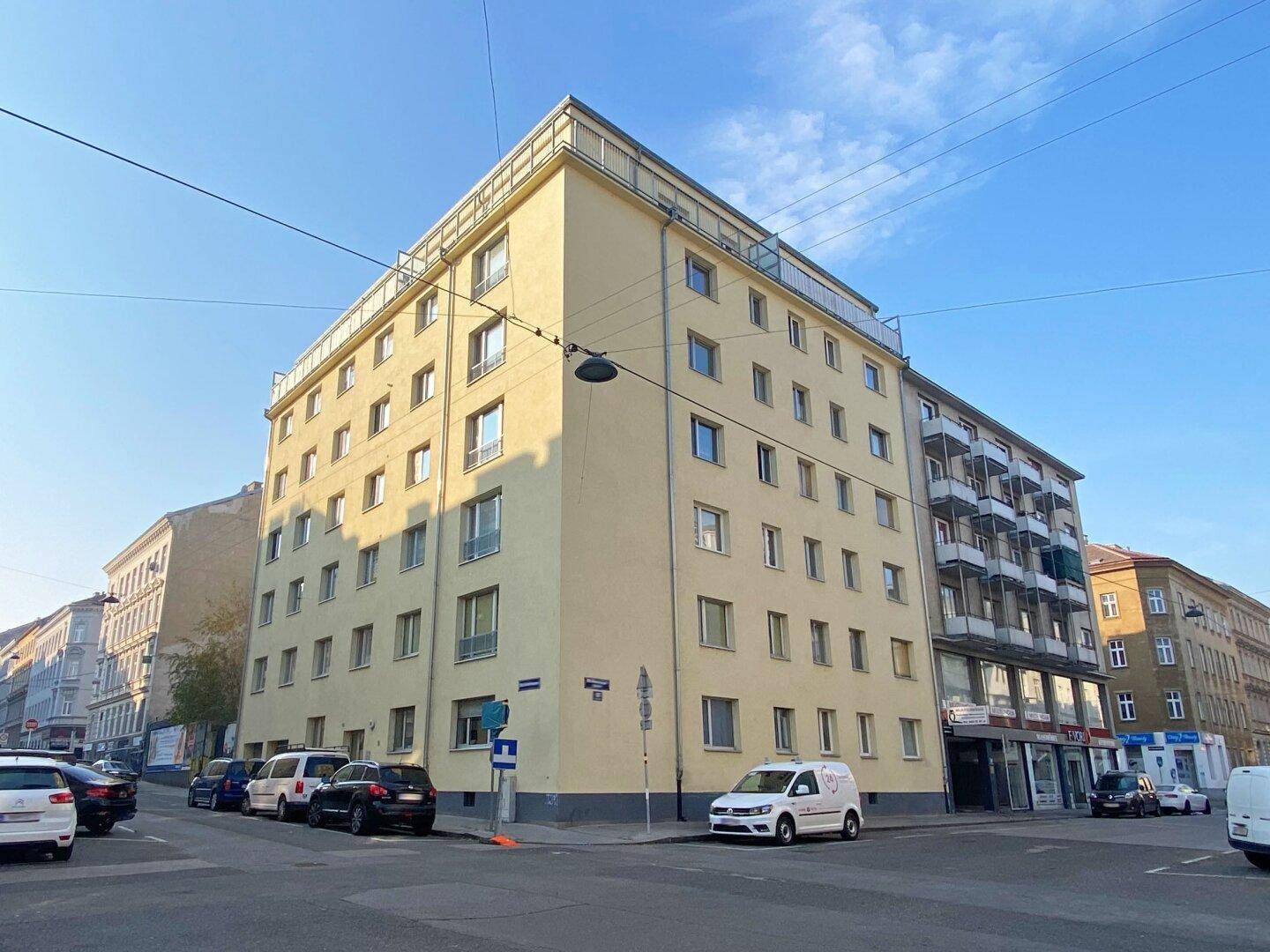 Mehrstöckiges Wohngebäude mit gelber Fassade und vielen Fenstern an einer städtischen Kreuzung.