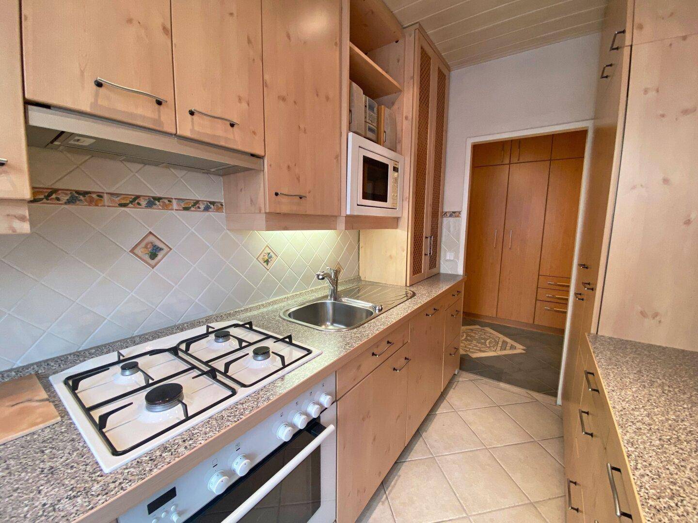 Funktionale Küche mit Holzschränken, Granitarbeitsplatte und Gasherd, ausgestattet mit Einbaugeräten.