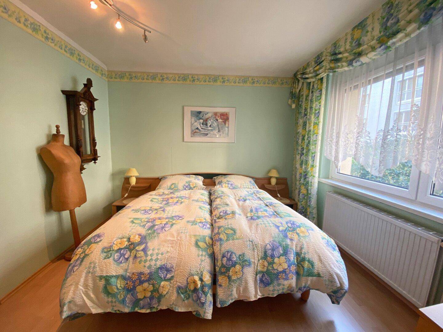 Helles Schlafzimmer mit Doppelbett, Holzfußboden und floraler Bordüre an den Wänden.