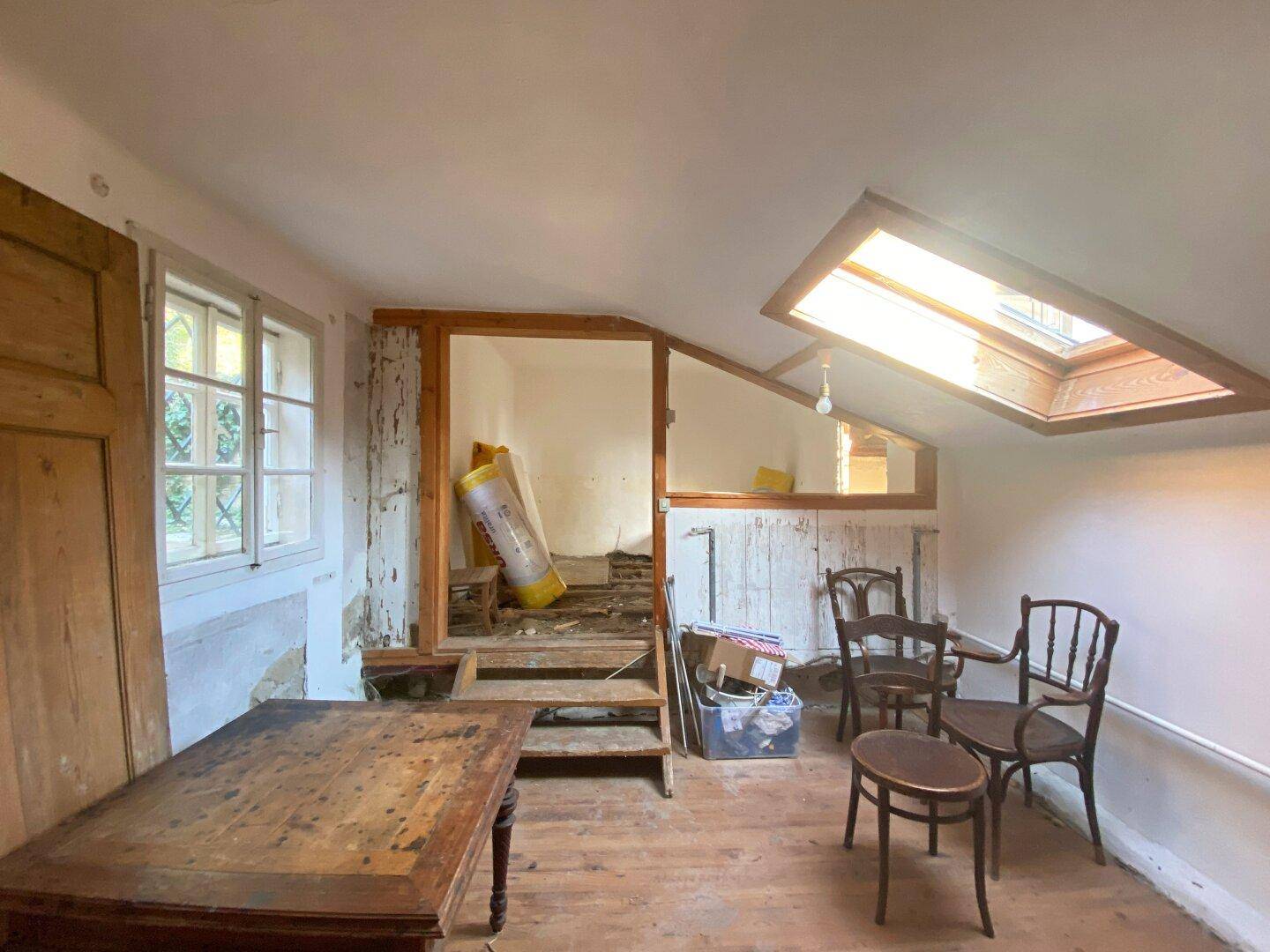 Dachgeschossraum in Renovierung mit Dachfenster, Holzboden und alten Möbeln.