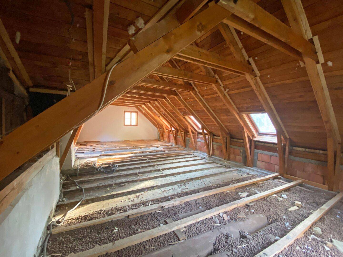 Geräumiger Dachboden in Renovierung mit sichtbaren Holzbalken und mehreren Dachfenstern.
