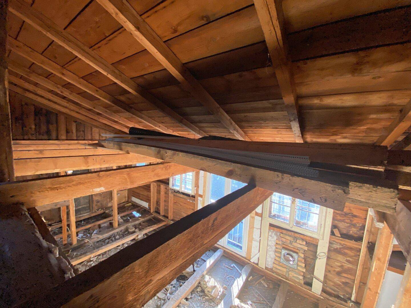 Blick in die offene Dachkonstruktion mit sichtbaren Holzbalken und Sparren.