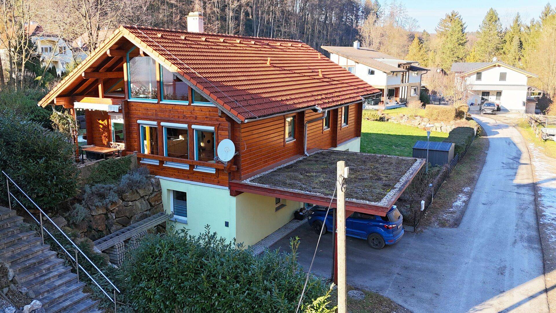 Holzhaus mit großzügigem Carport und begrüntem Dach in ländlicher Umgebung.