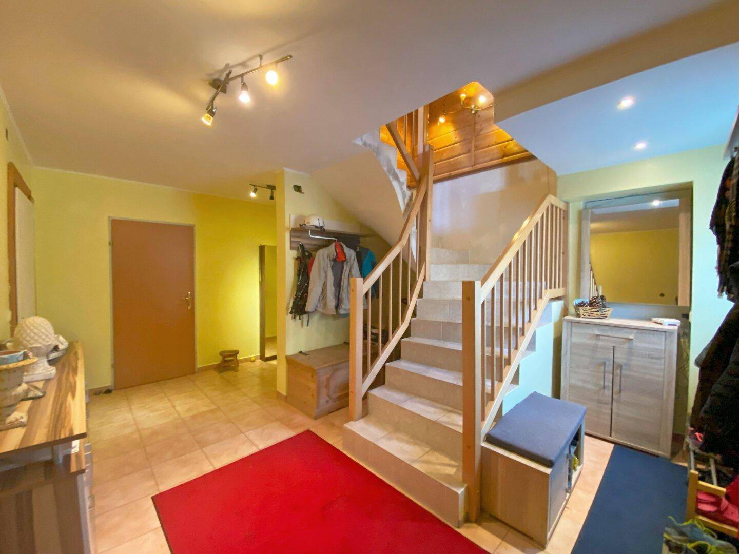 Heller Eingangsbereich mit gefliestem Boden, Garderobe und Holztreppe zum Obergeschoss.
