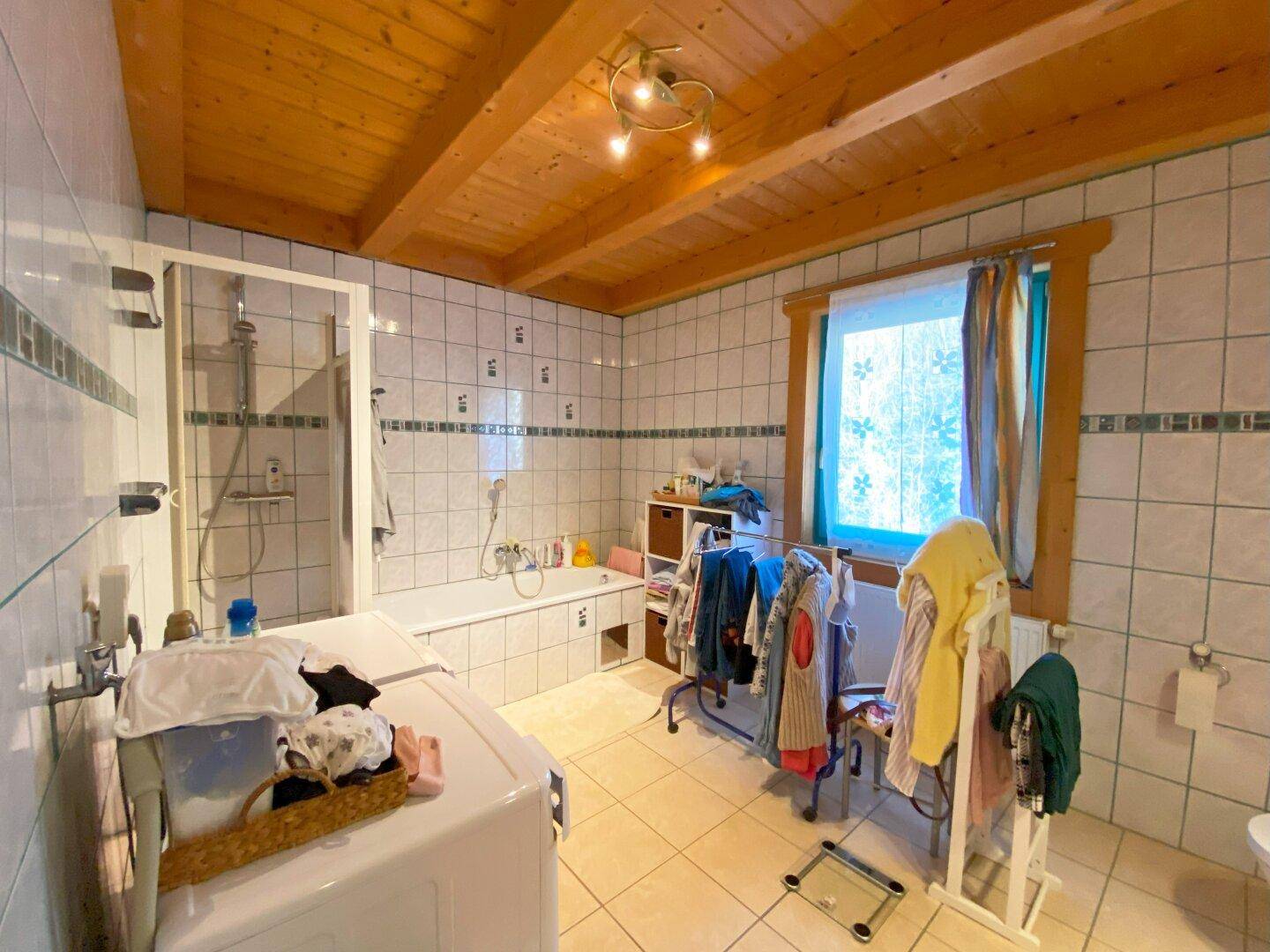 Helles Badezimmer mit Badewanne, Duschbereich und Fenster, komplett gefliest.