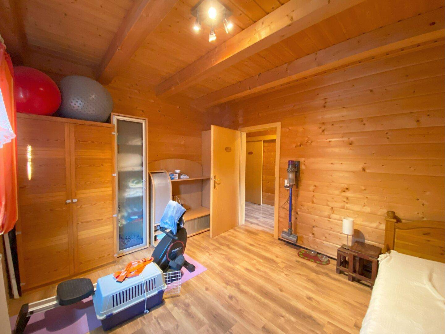 Schlafzimmer mit Holzwänden, Holzbalkendecke und Platz für Sportgeräte und Stauraum.