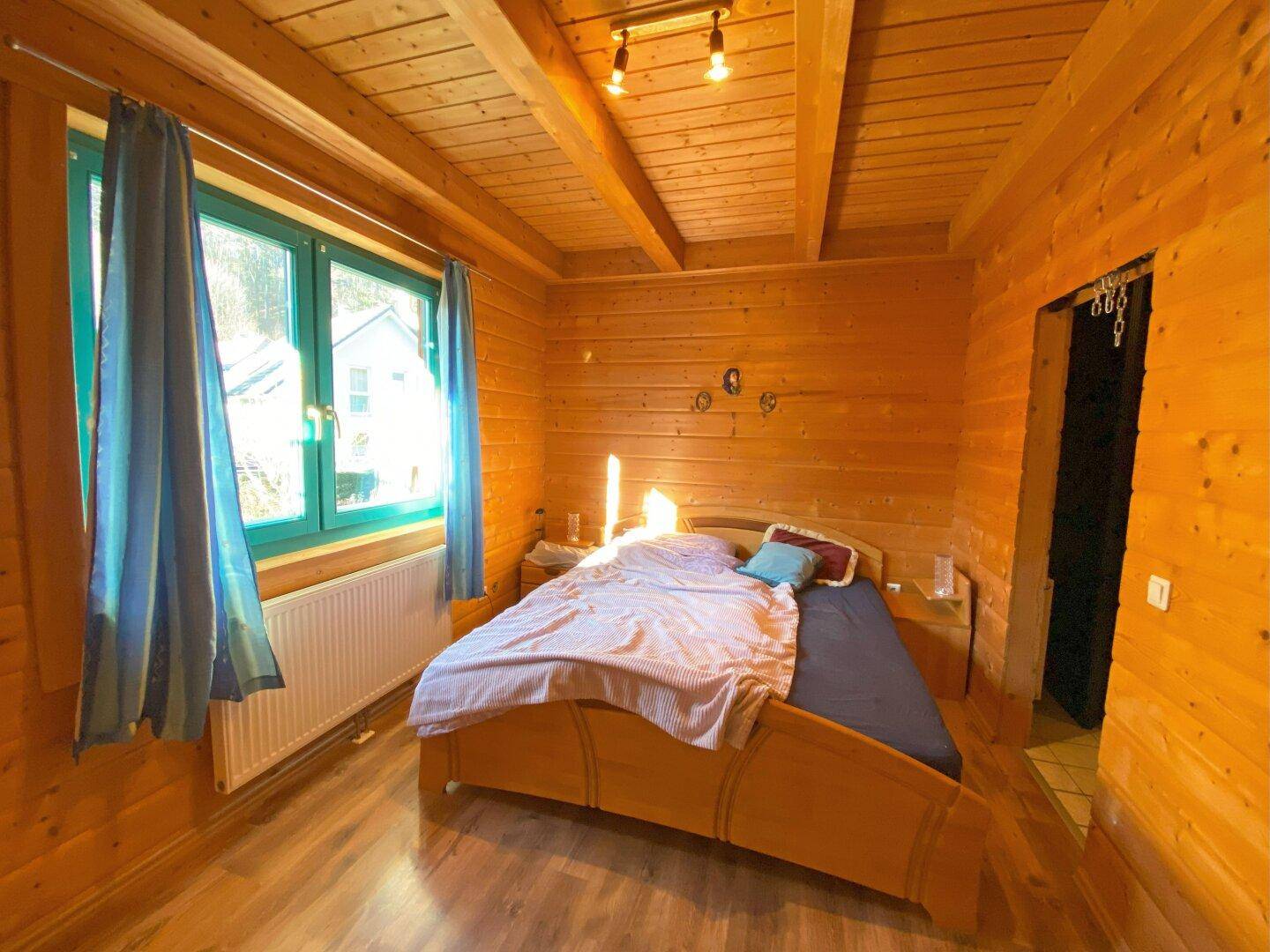 Gemütliches Schlafzimmer mit Holzwänden, Holzboden und großem Fenster für viel Licht.