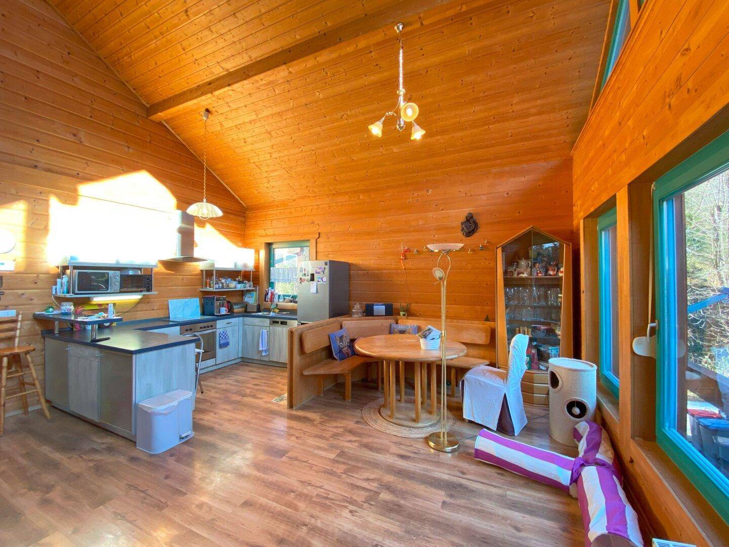 Offene Wohnküche mit Essbereich, Holzwänden und großen Fenstern, die viel Licht hereinlassen.