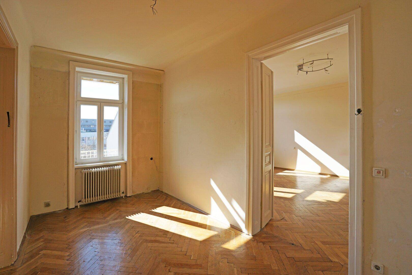 Heller Raum mit Fischgrätparkett und einem großen Fenster, das den Blick nach draußen freigibt.