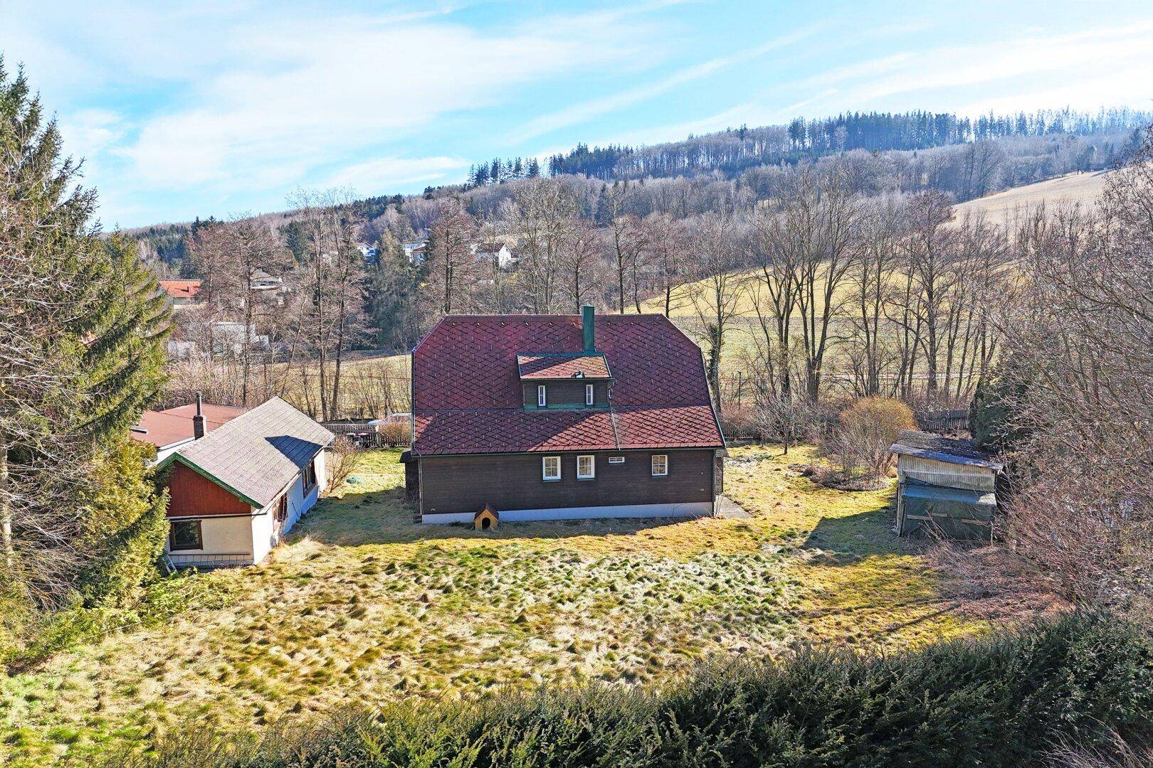 Rückansicht des Hauses mit weitläufiger Rasenfläche und Blick auf die umliegende Hügellandschaft.
