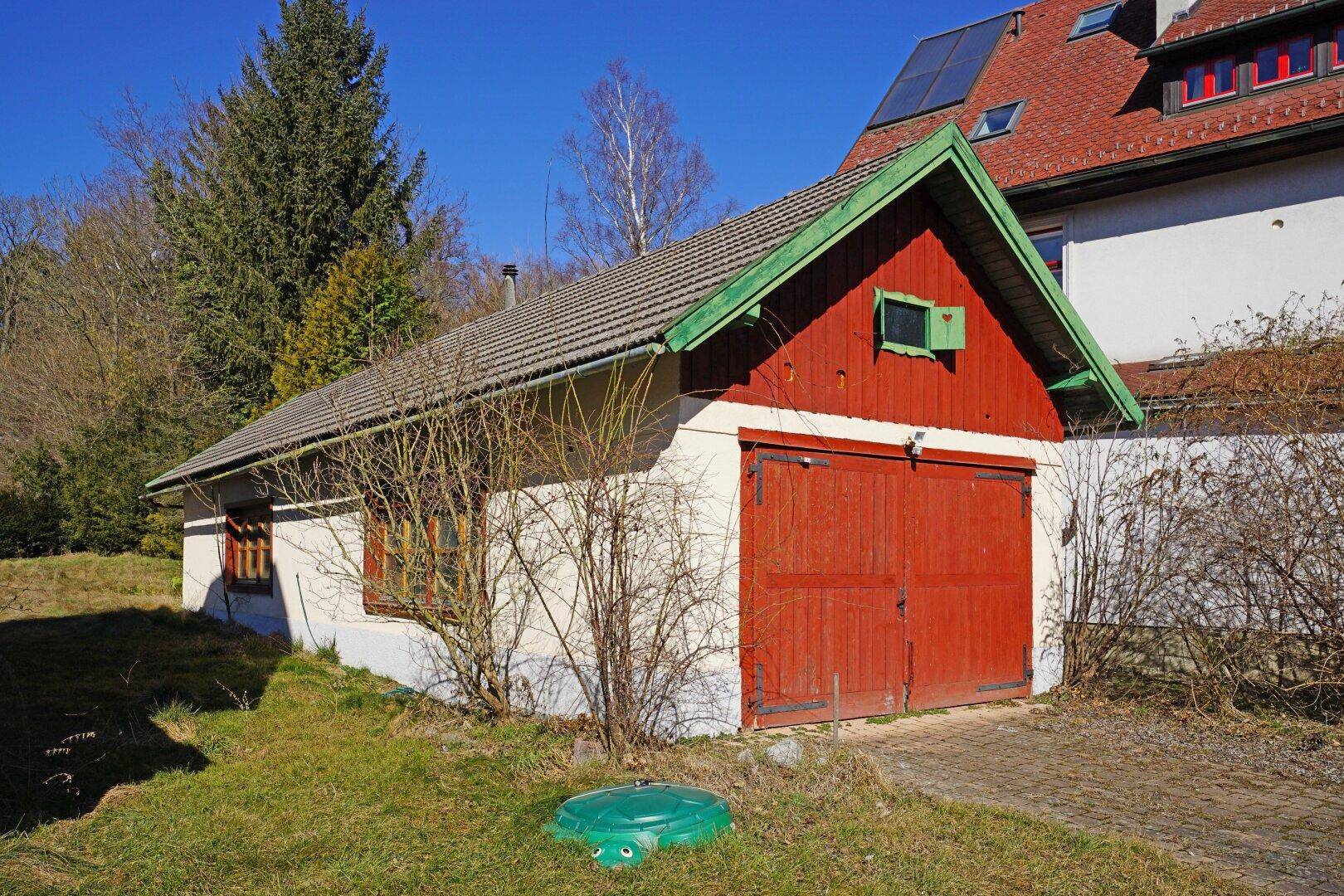 Separate Garage mit roten Holztoren und einem Satteldach neben dem Haupthaus auf dem Grundstück.