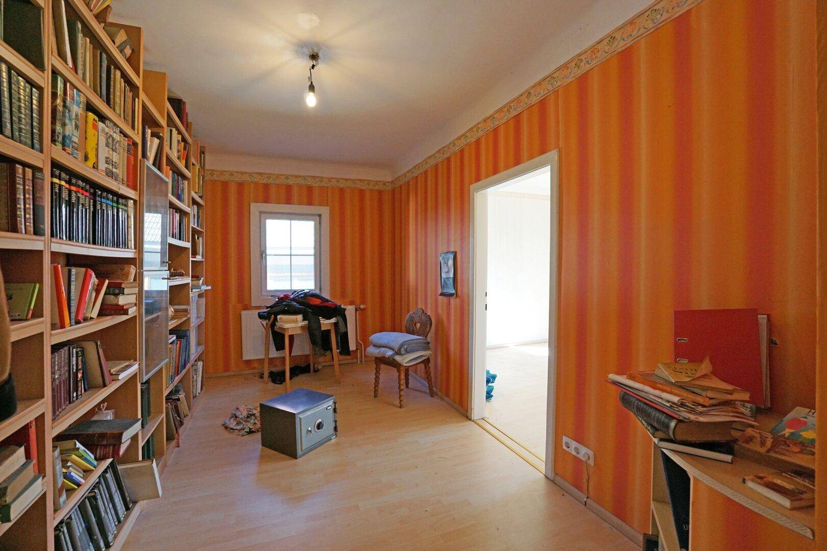 Arbeitszimmer mit Bücherregalen, orange gestreiften Tapeten und hellem Laminatboden für eine gemütliche Atmosphäre.