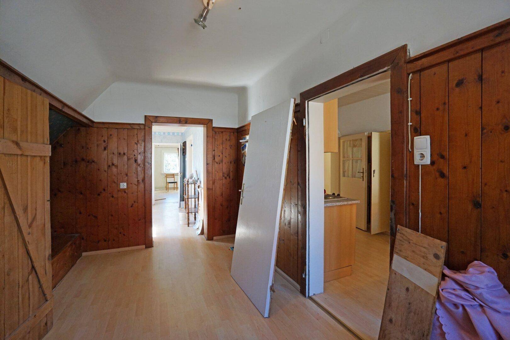 Flur mit Holzvertäfelung und Zugang zu mehreren Zimmern, teilweise mit Holztüren und hellem Boden.