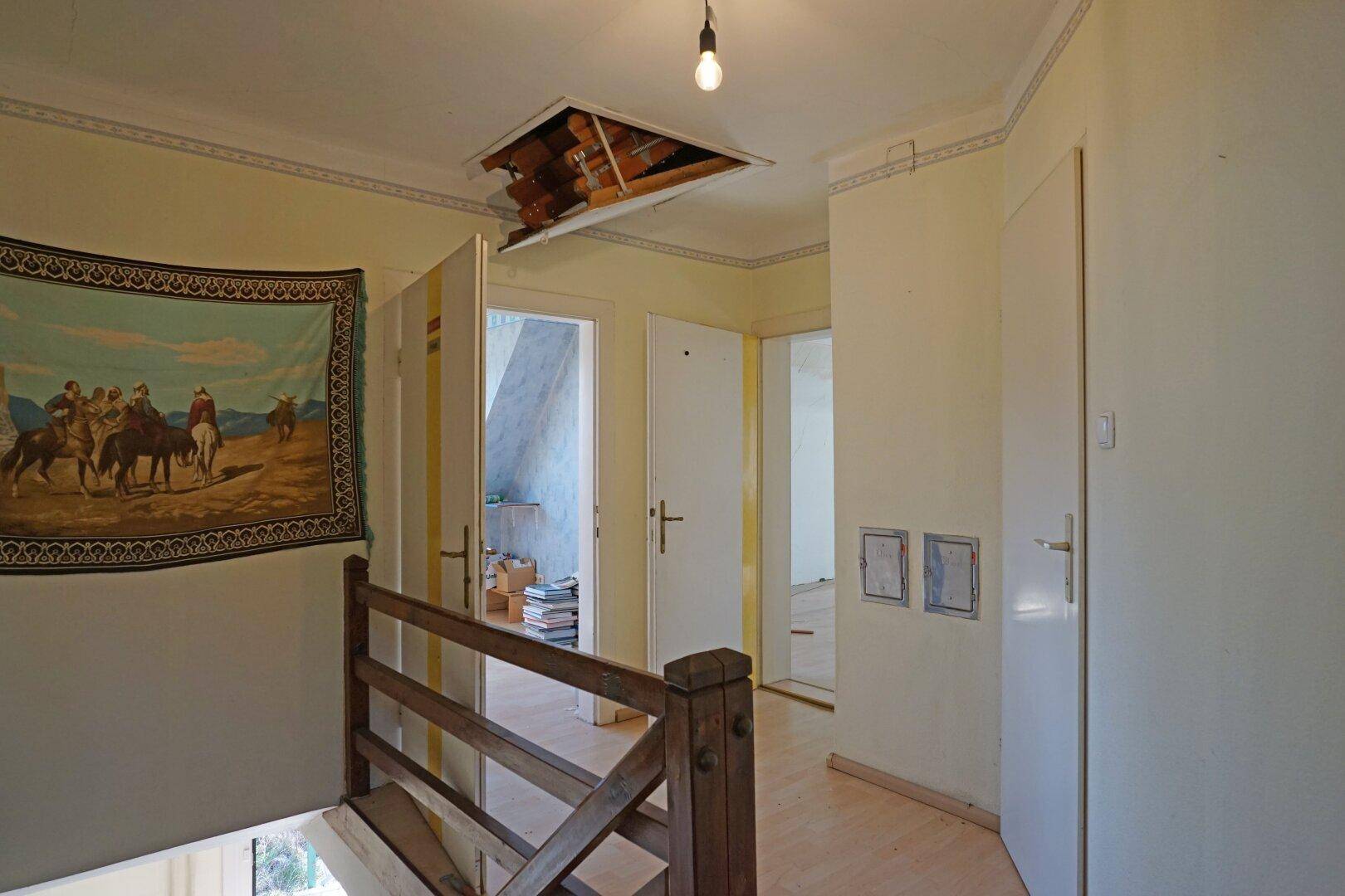 Obergeschoss-Flur mit Holzgeländer und Zugang zu weiteren Räumen, inklusive einer Dachbodenluke.