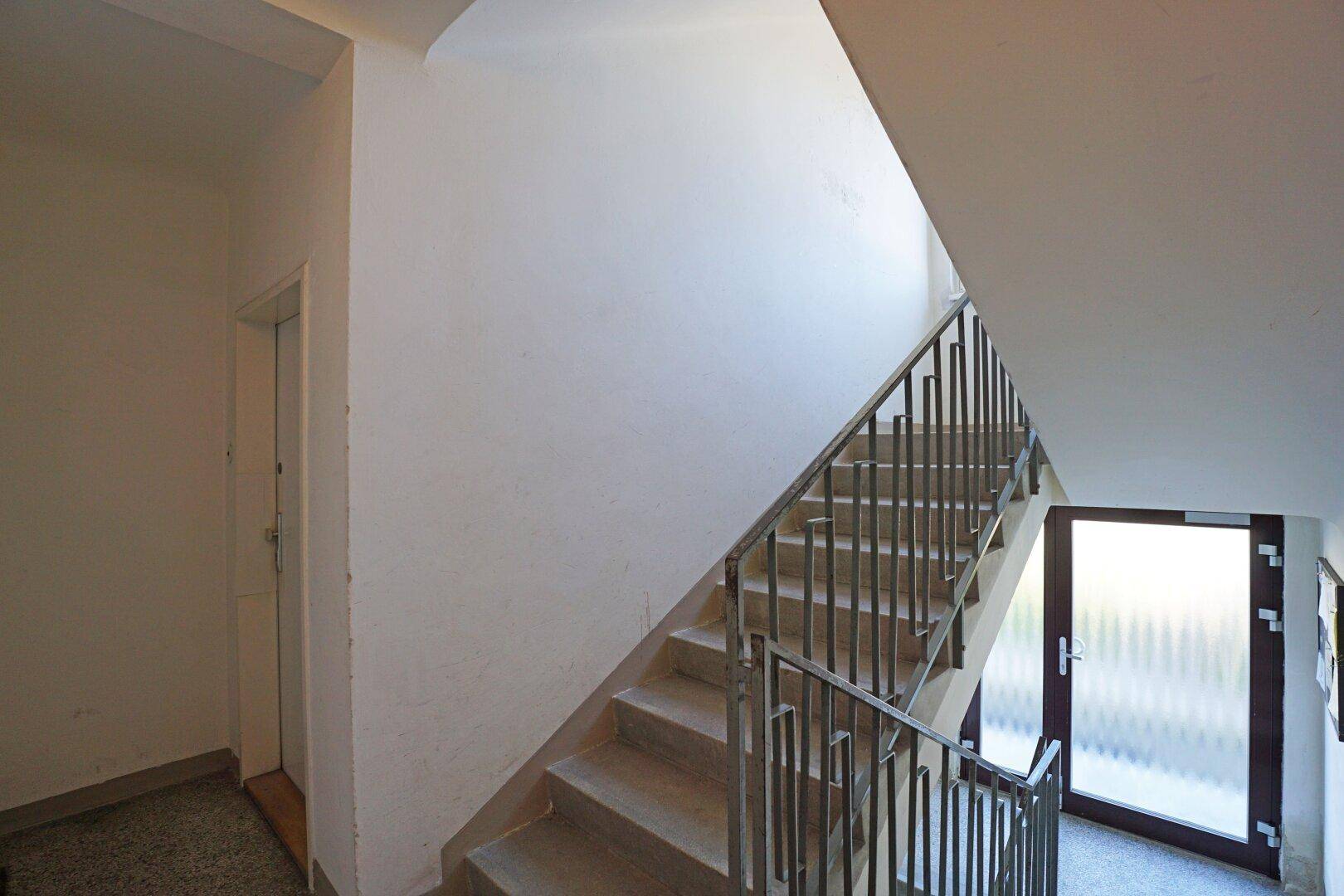 Treppenhaus mit hellem Treppenaufgang und Metallgeländer, das zu den oberen Etagen führt.