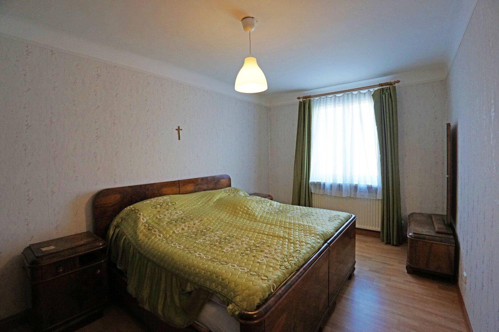 Schlafzimmer mit Holzbett, Laminatboden und Fenster mit Vorhängen.