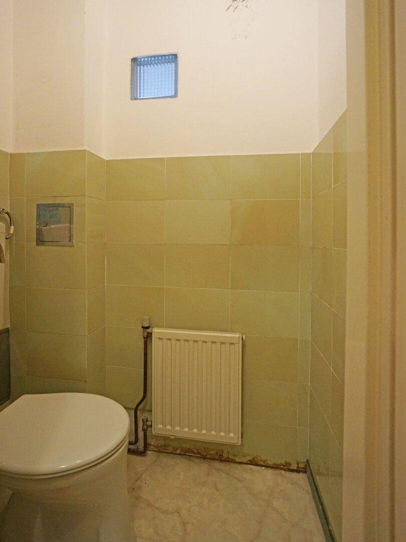 Separate Toilette mit hellgrünen Fliesen und kleinem Fenster für Belüftung.