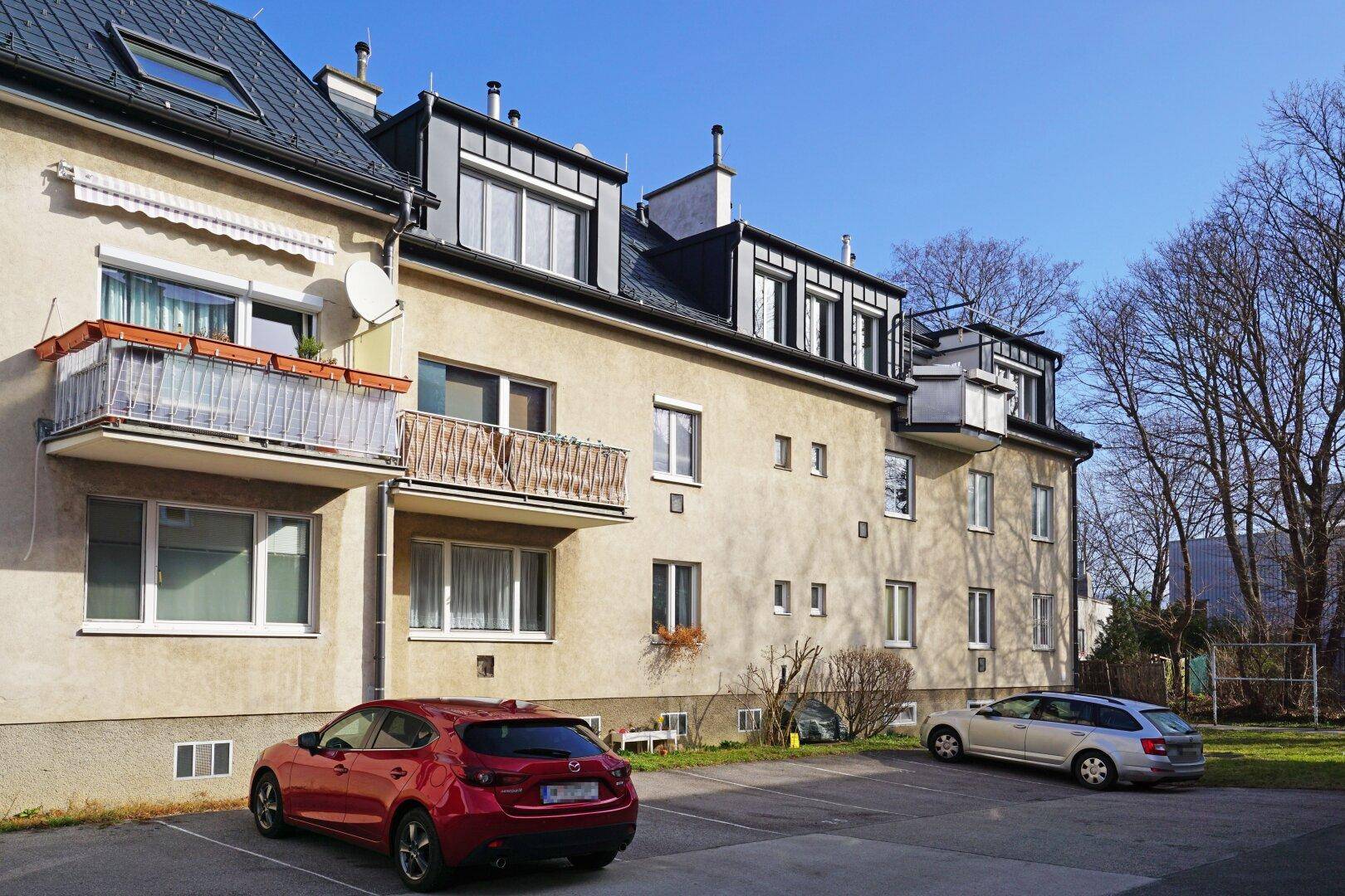 Außenansicht eines Wohngebäudes mit Balkonen und Parkplätzen im Freien.