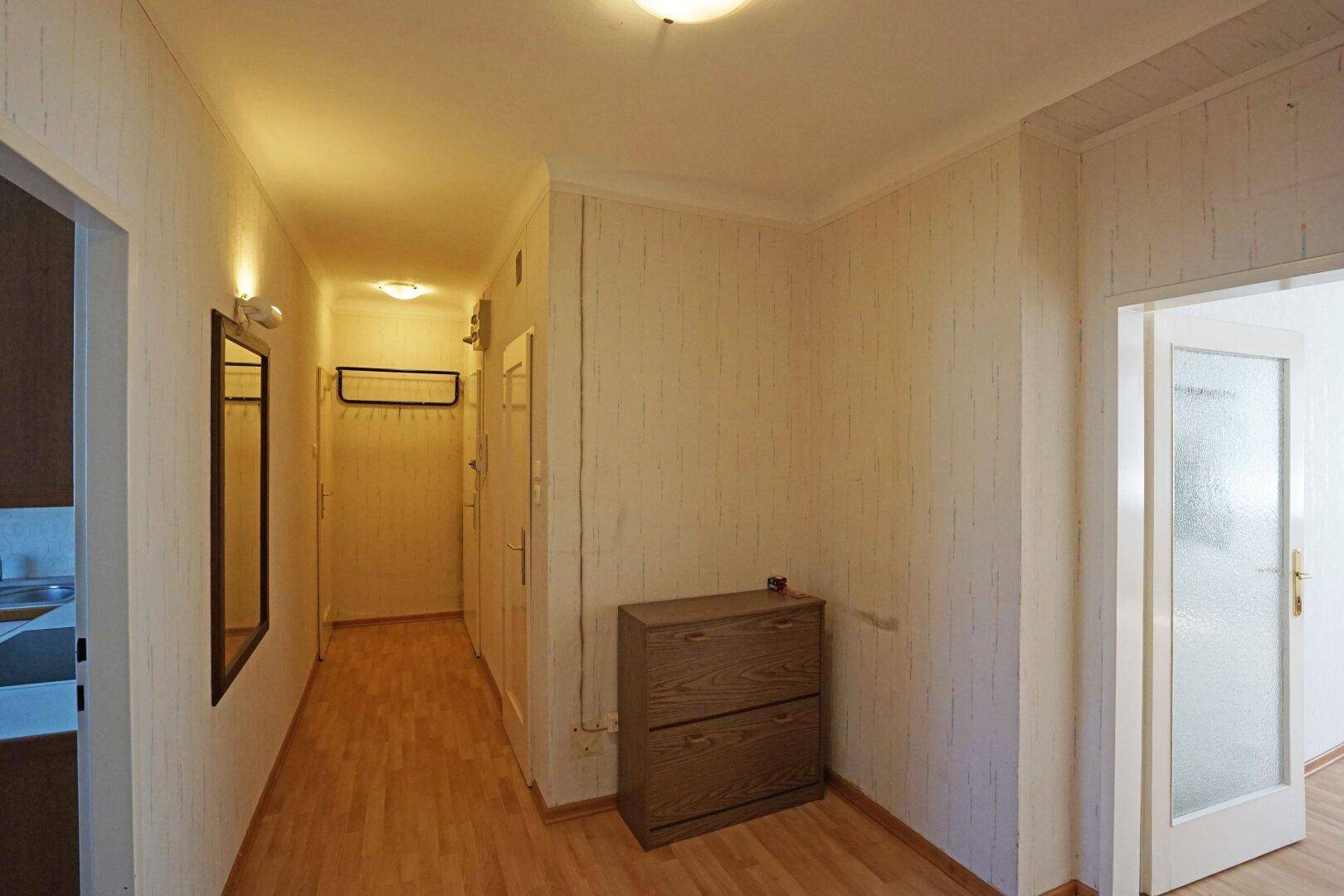 Heller Flur mit Laminatboden, Spiegel und Garderobe, der zu weiteren Räumen führt.
