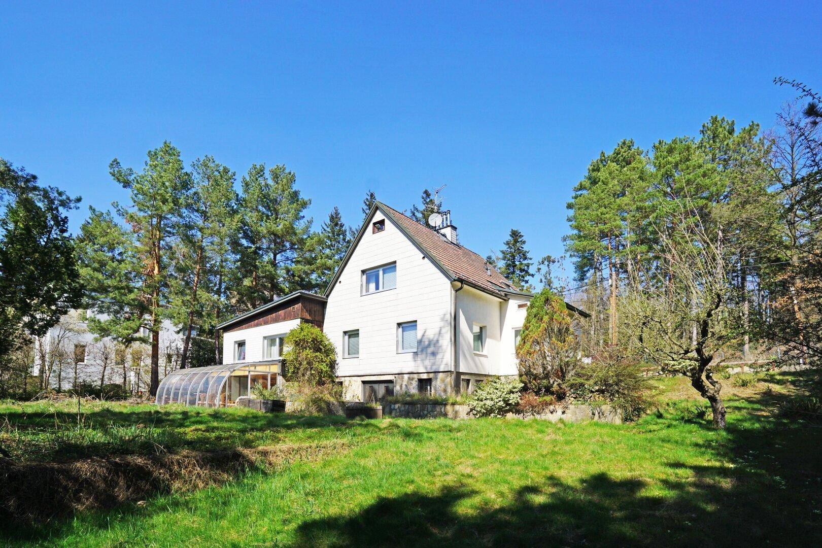 Freistehendes Haus mit Wintergarten und großem Gartenbereich, eingebettet in grüne Natur.