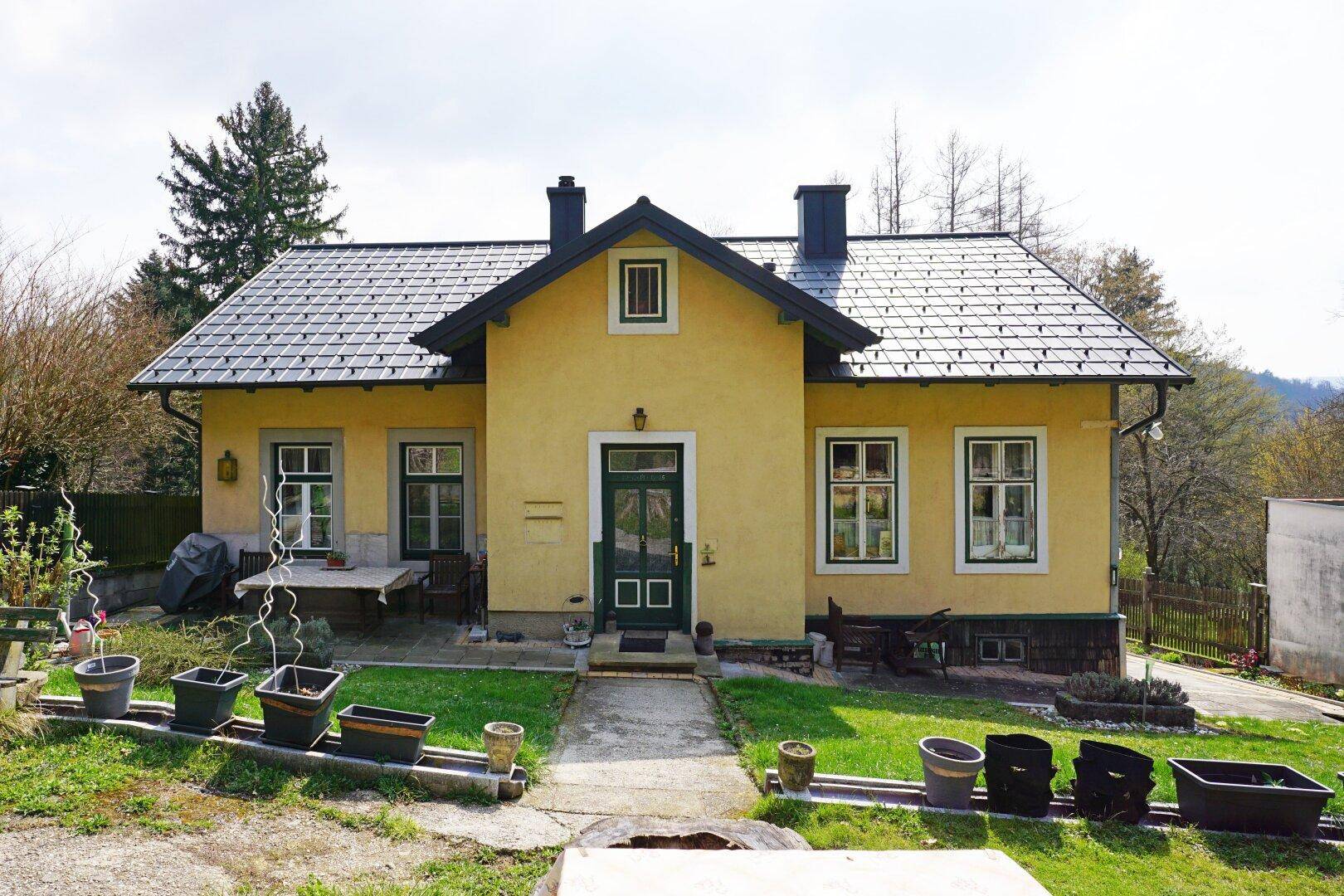 Vorderansicht eines charmanten gelben Hauses mit dunklem Dach und gepflegtem Vorgarten.