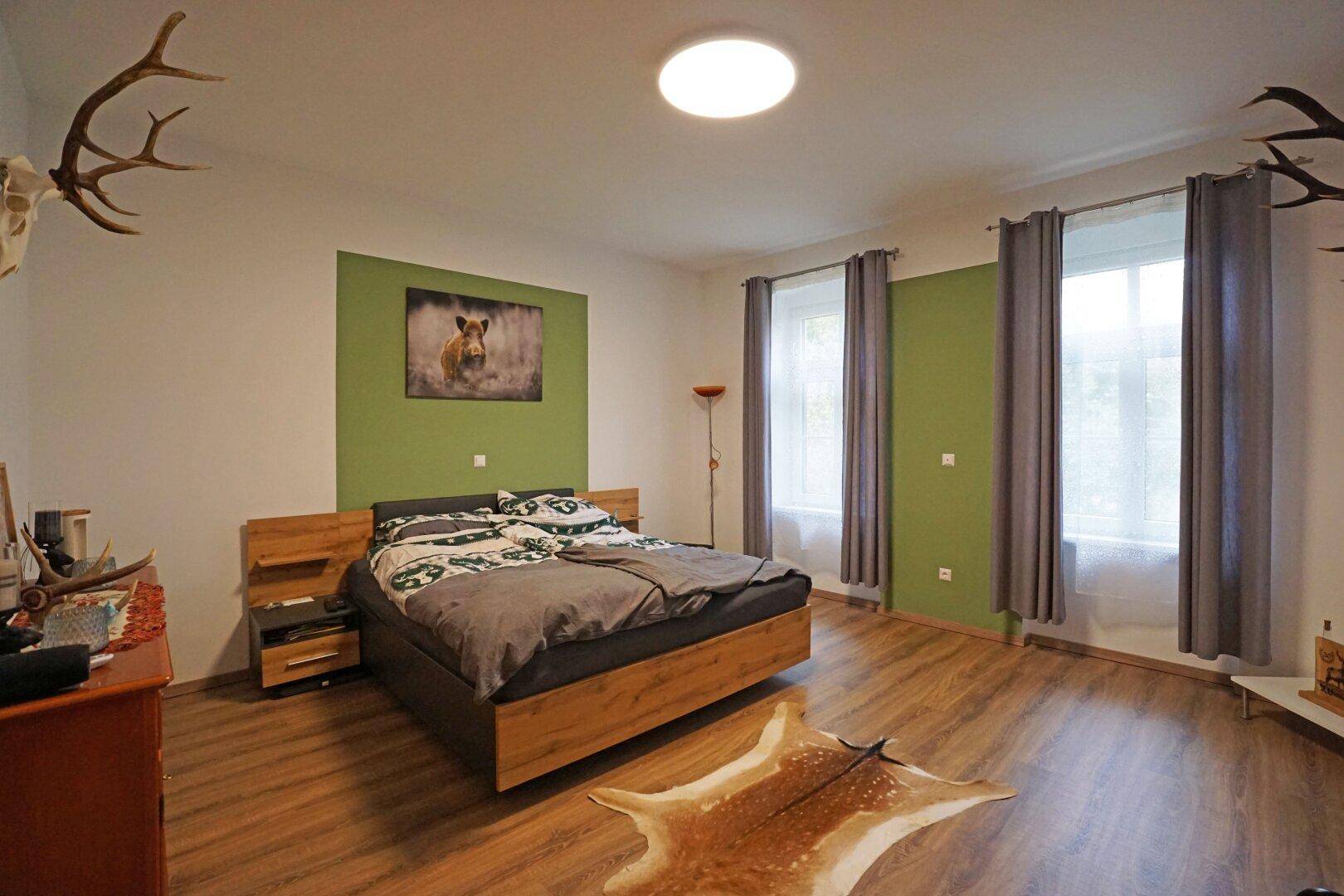 Geräumiges Schlafzimmer mit Holzboden, grünen Akzentwänden und Hirschgeweih-Dekoration.