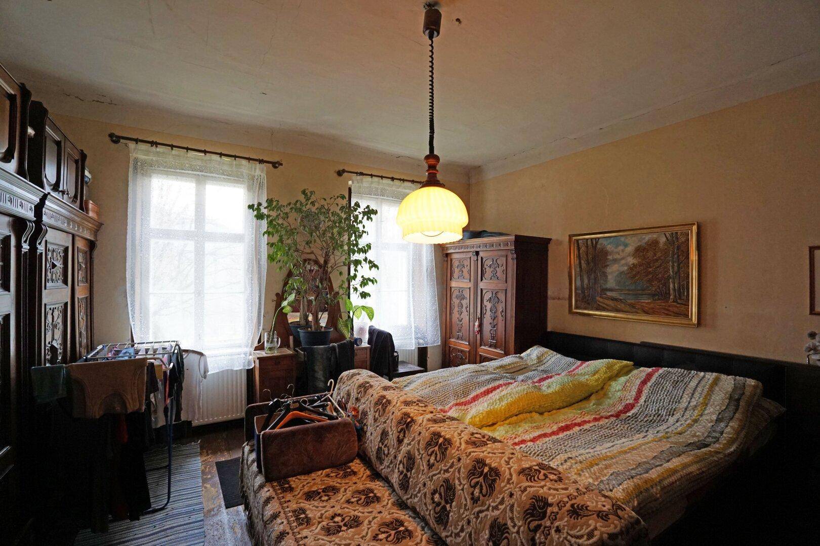 Schlafzimmer mit traditionellen Holzmöbeln, zwei Fenstern und einem gemütlichen Bett.