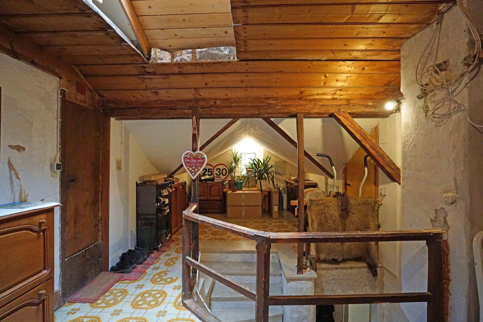 Rustikaler Dachboden mit sichtbaren Holzbalken, Treppenzugang und Stauraum.