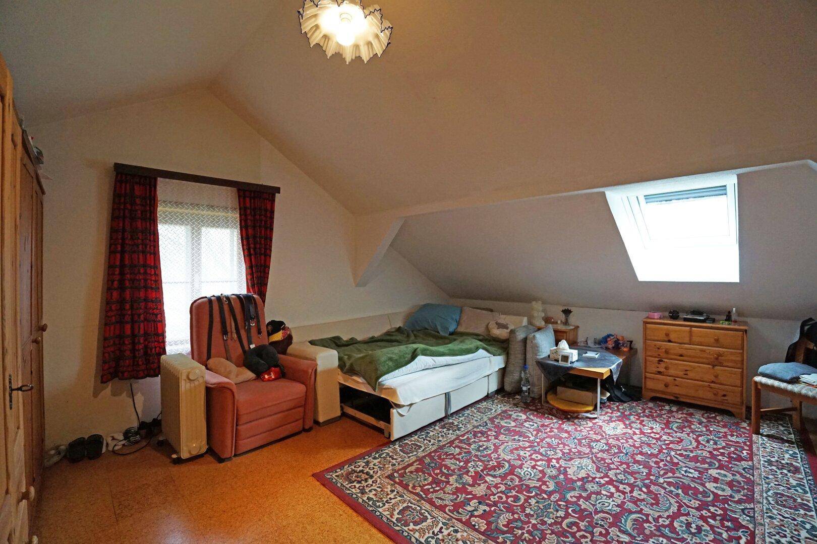 Gemütliches Schlafzimmer im Dachgeschoss mit Dachfenster, Teppich und Bett.