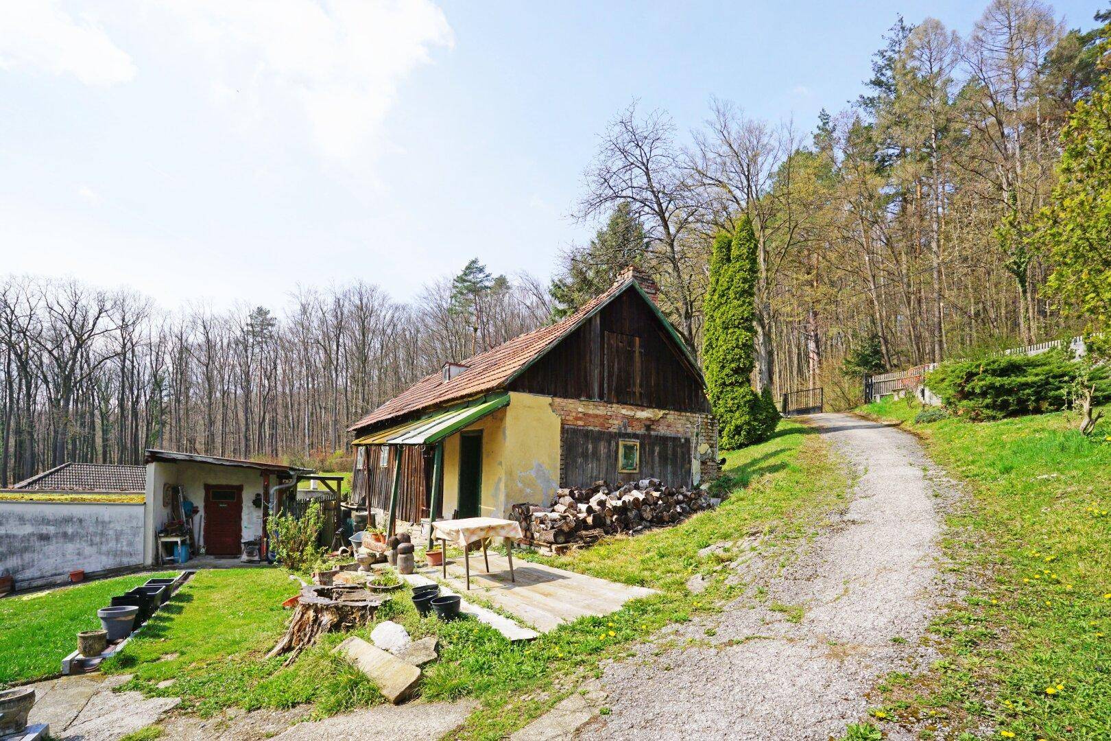 Rustikales Gebäude mit Holzelementen und einem unbefestigten Weg, umgeben von Natur.