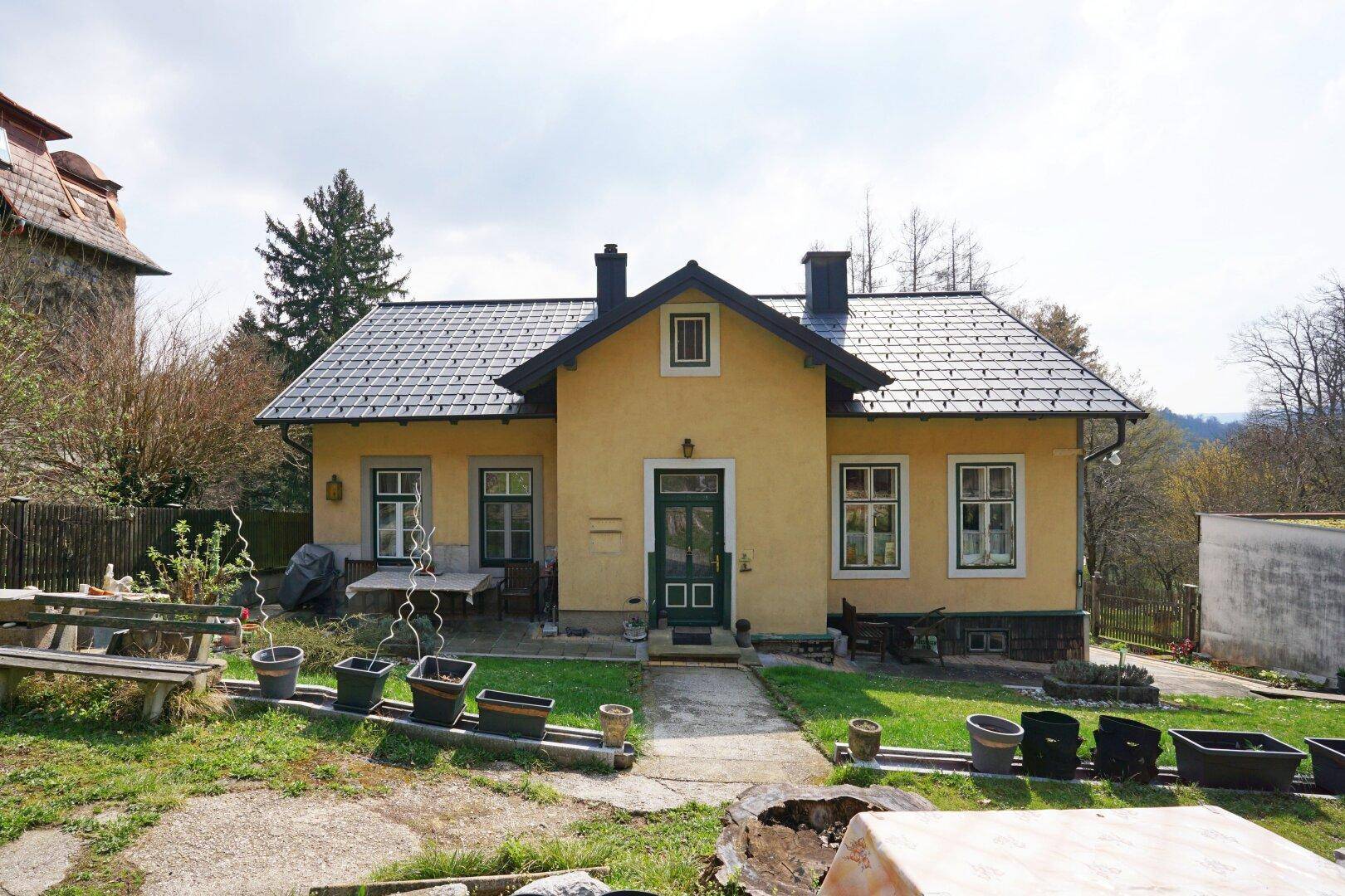 Gelbes Einfamilienhaus mit dunklem Ziegeldach und einem kleinen Vorgarten in ländlicher Umgebung.