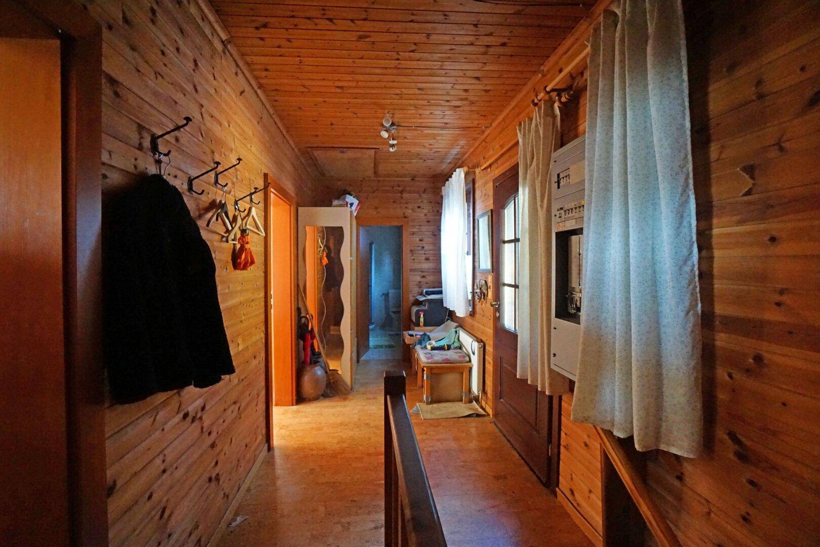 Rustikaler Flur mit Holzvertäfelung an Wänden und Decke sowie einem Fenster mit Vorhängen.