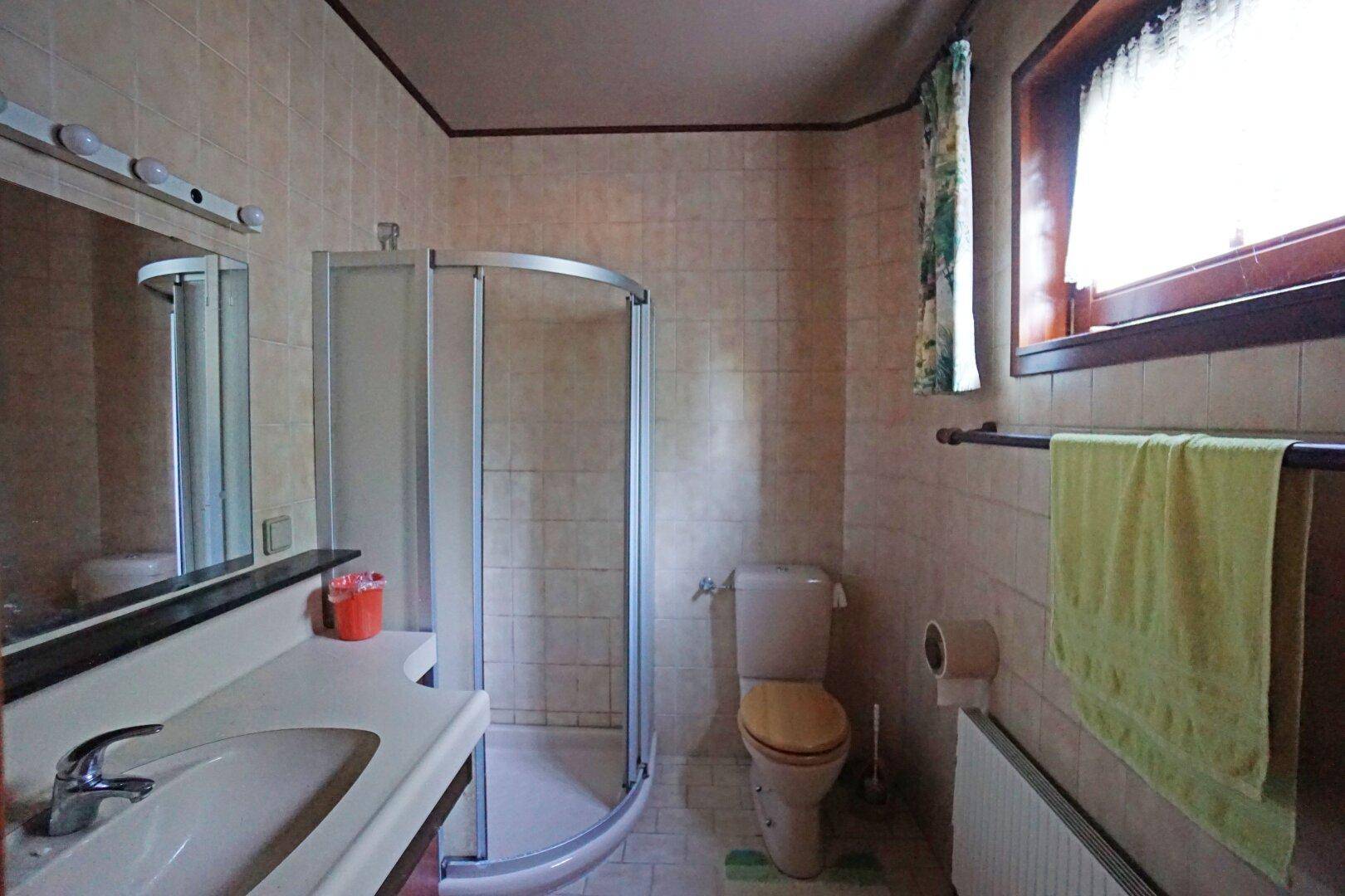 Badezimmer mit Duschkabine, WC, Waschbecken und Fenster, gefliest in beigen Tönen.
