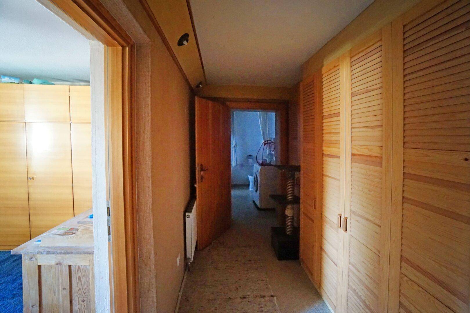 Flur mit Holzschränken und Zugang zu weiteren Räumen, der in einen Waschraum führt.