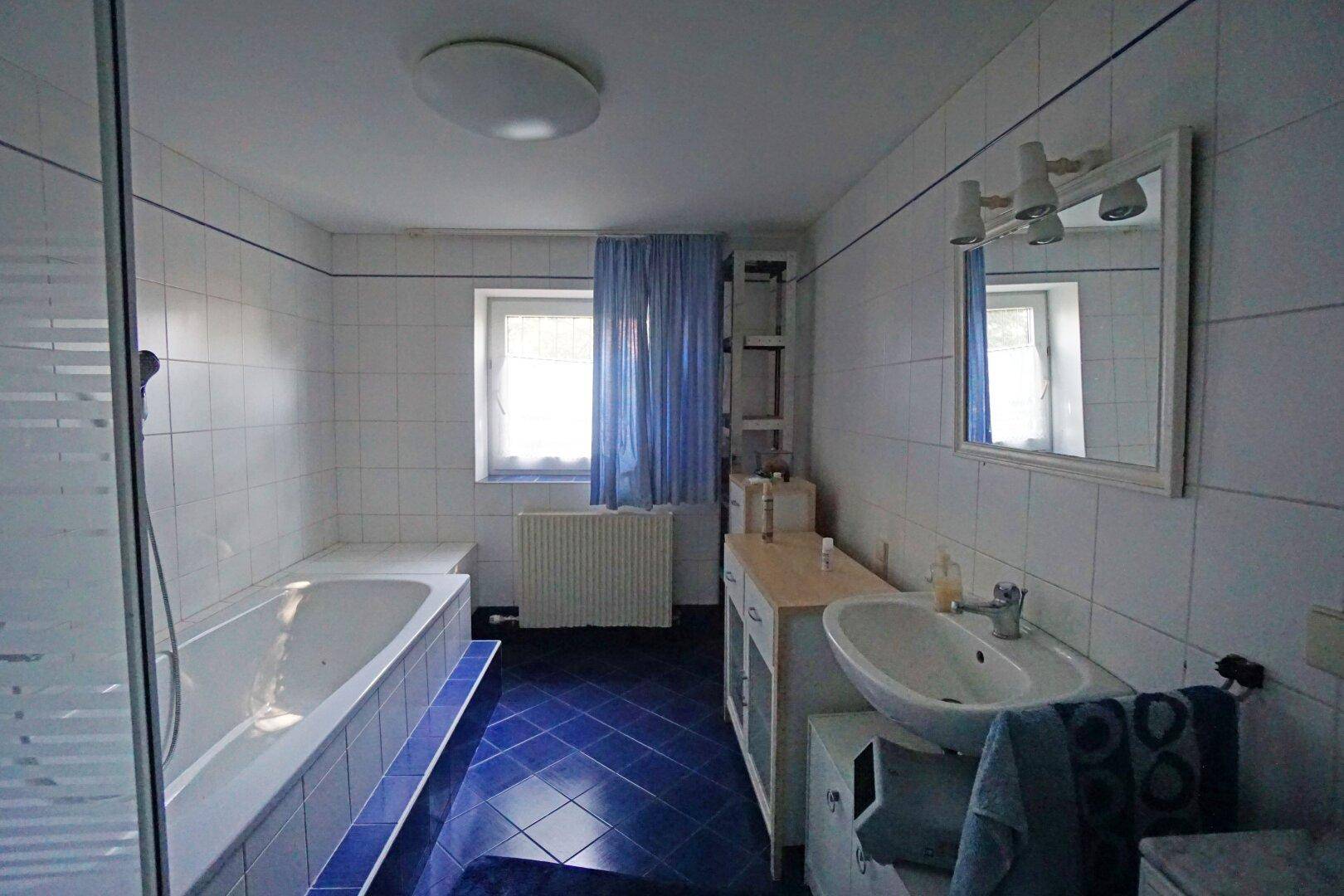 Geräumiges Badezimmer mit Badewanne, Duschkabine, Waschbecken und blauen Bodenfliesen.