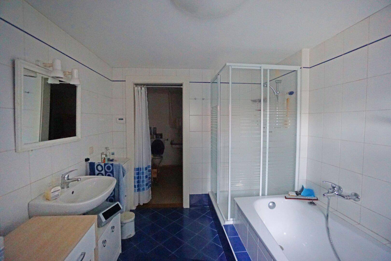 Badezimmer mit Badewanne, Duschkabine und Waschbecken, durch eine Tür mit einem weiteren Raum verbunden.