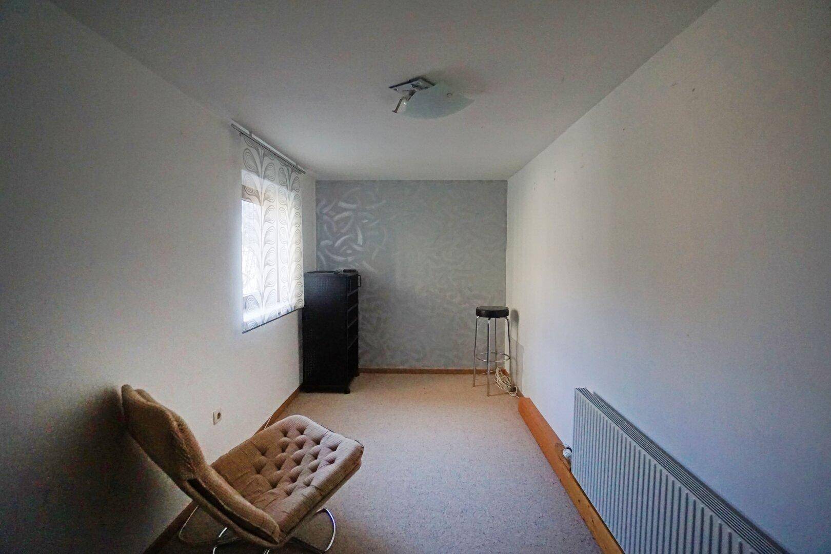 Helles Zimmer mit Teppichboden, einer Akzentwand und einem Fenster für natürliches Licht.