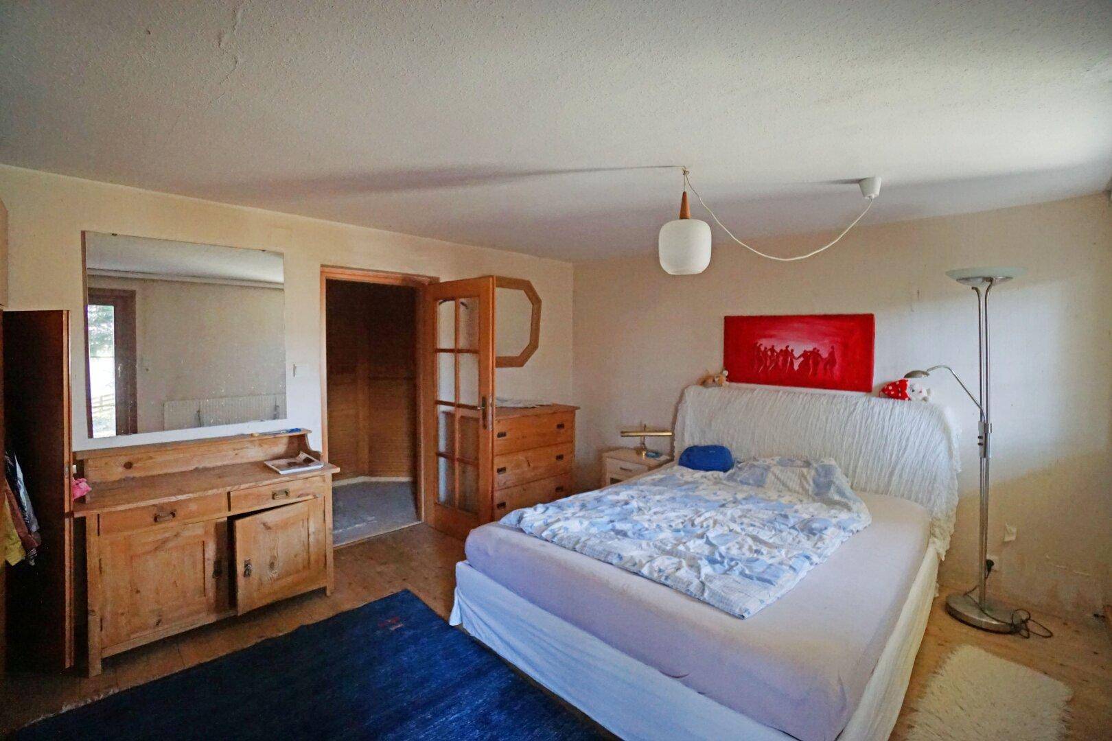 Schlafzimmer mit Holzboden, Bett und einem großen Spiegel, der den Raum optisch erweitert.