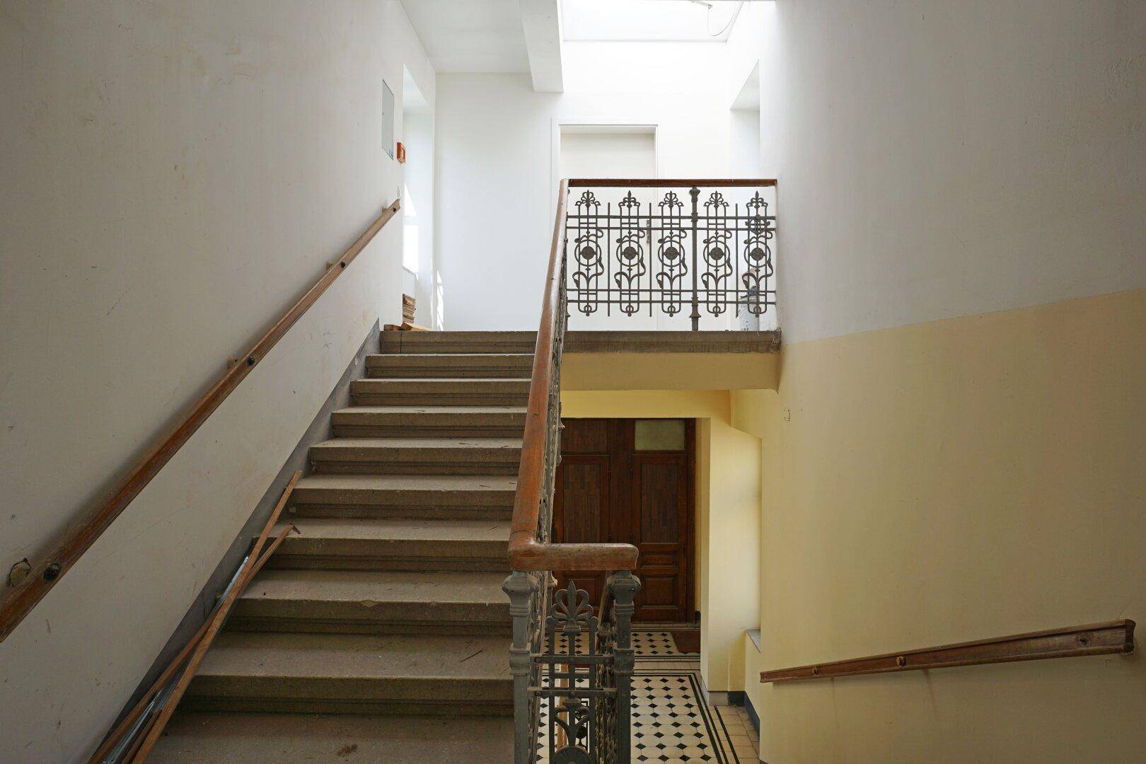 Historisches Treppenhaus mit schmiedeeisernem Geländer und Holzhandlauf, das den Charme des Altbaus bewahrt.