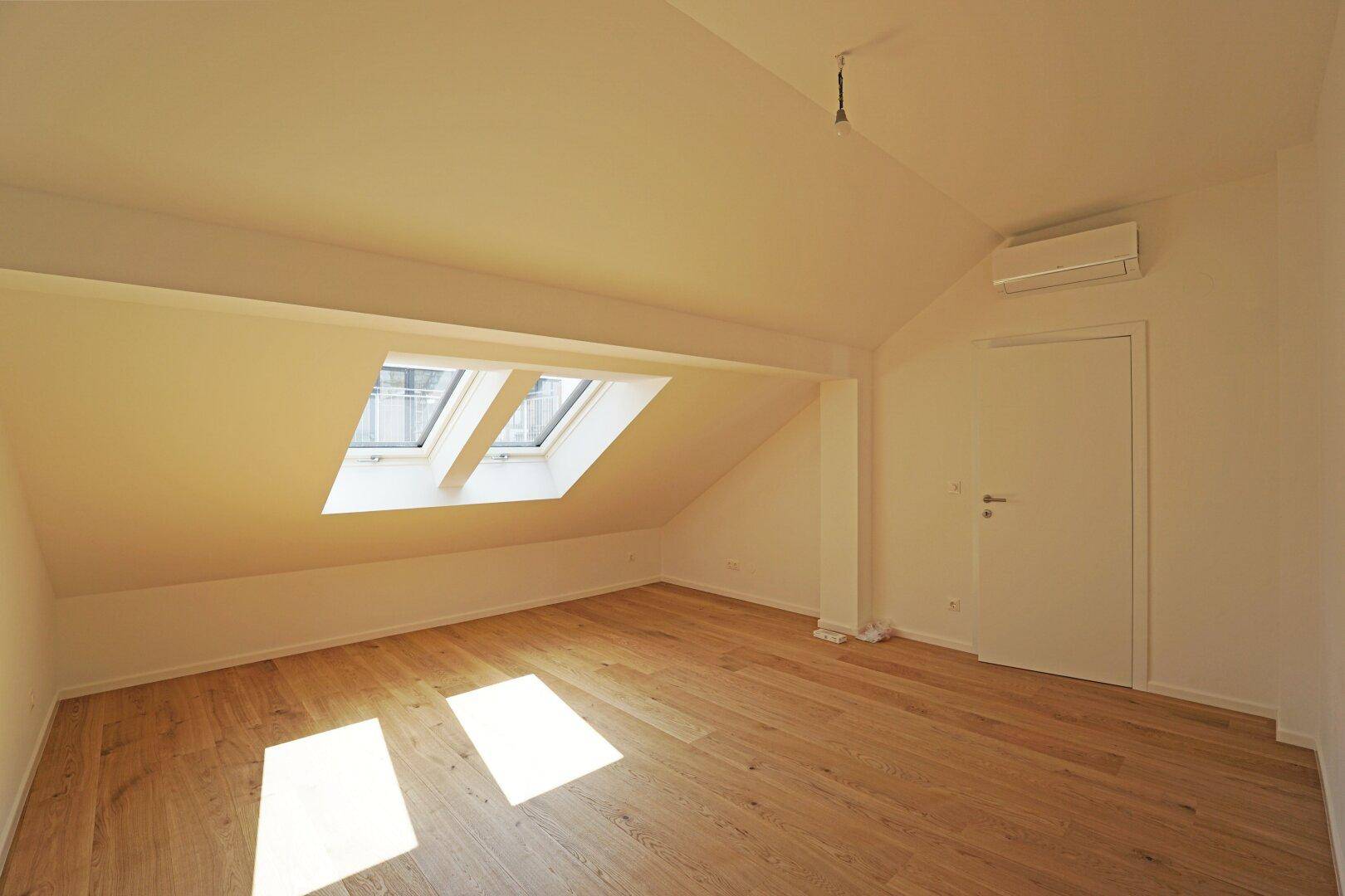 Helles Dachzimmer mit Holzboden, Dachfenstern und einer Klimaanlage für Komfort.