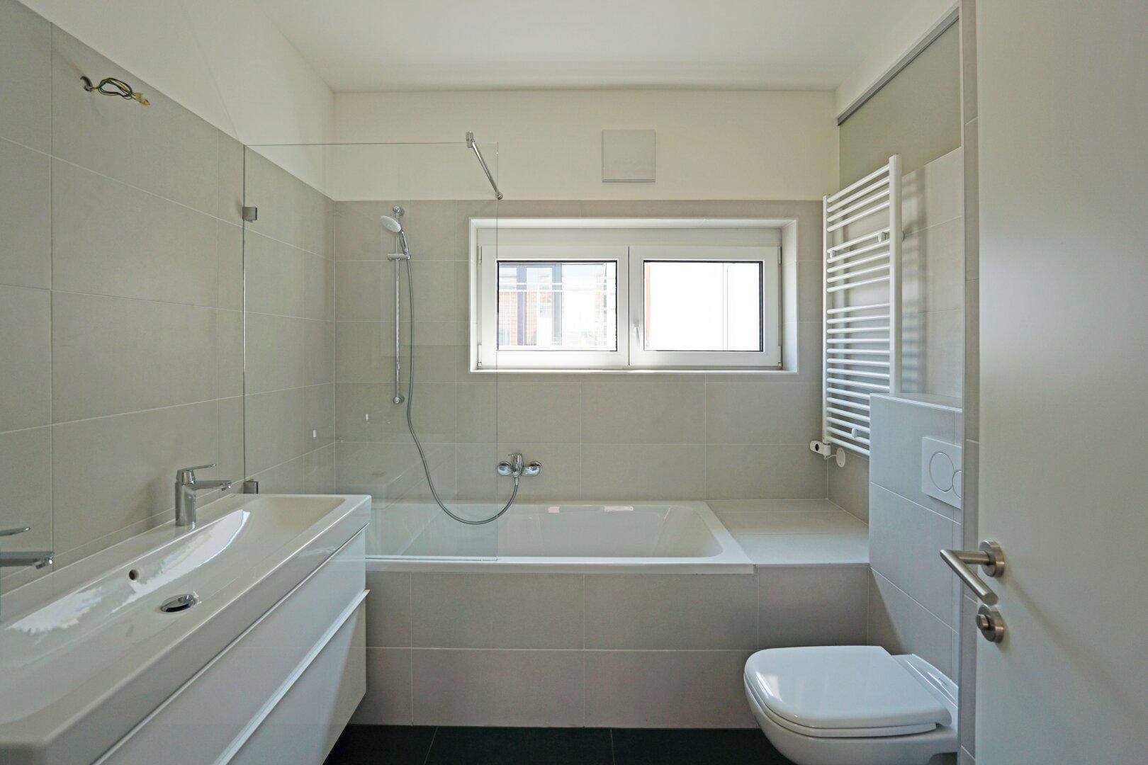 Modernes Badezimmer mit Badewanne, Dusche, WC und beheiztem Handtuchhalter.