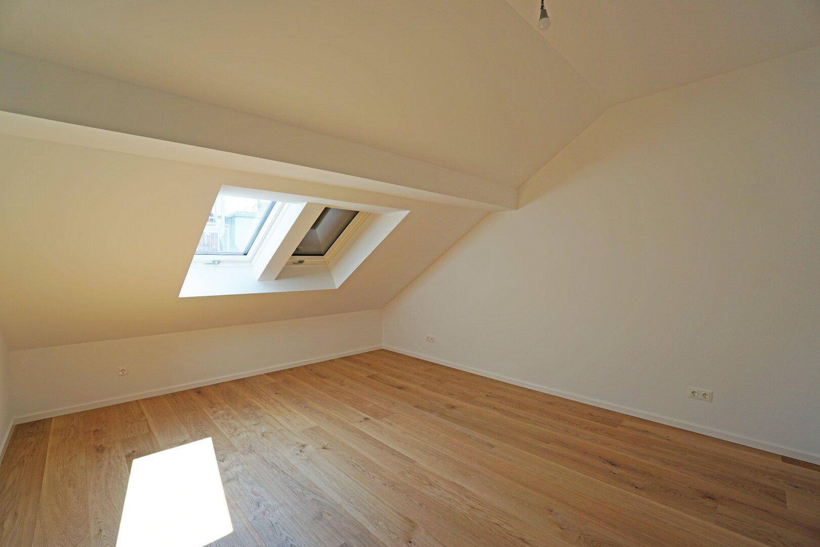 Gemütliches Dachzimmer mit Holzboden und einem Dachfenster, das für natürliche Belichtung sorgt.