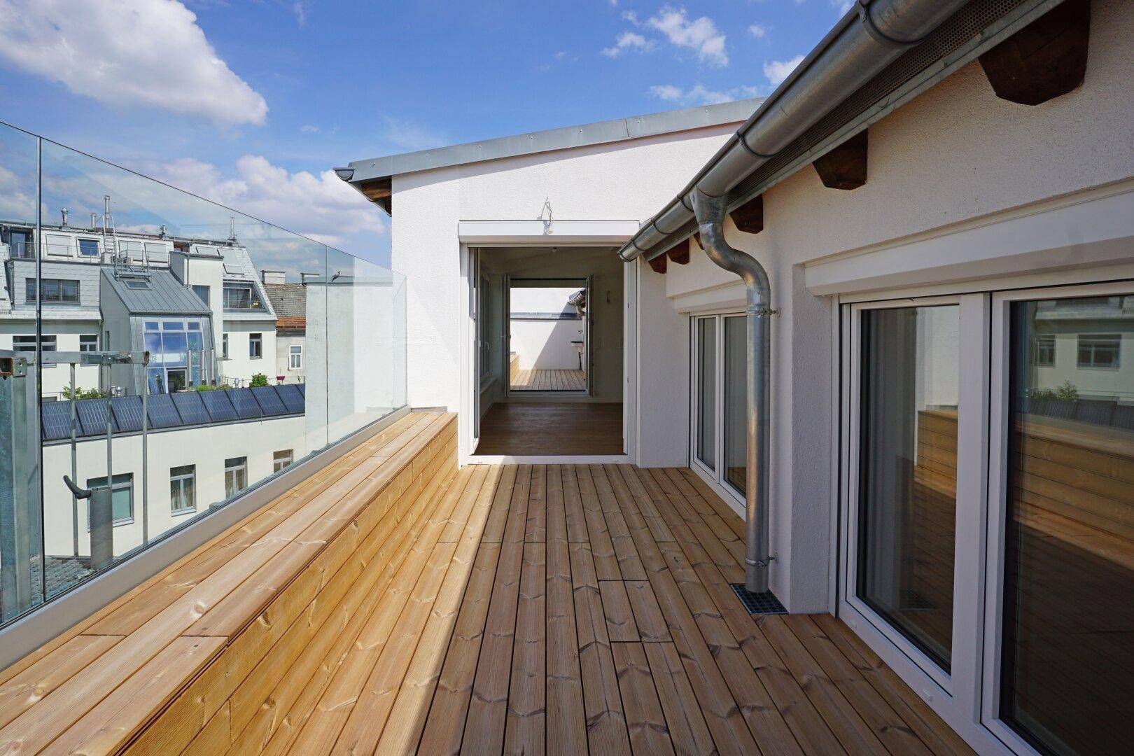 Geräumige Dachterrasse mit Holzbelag und Glasgeländer, bietet Zugang zu den Innenräumen.
