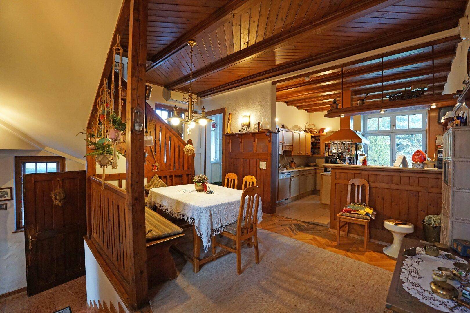 Rustikaler Essbereich mit Holzbalkendecke, Holztisch und Blick in die traditionelle Küche.